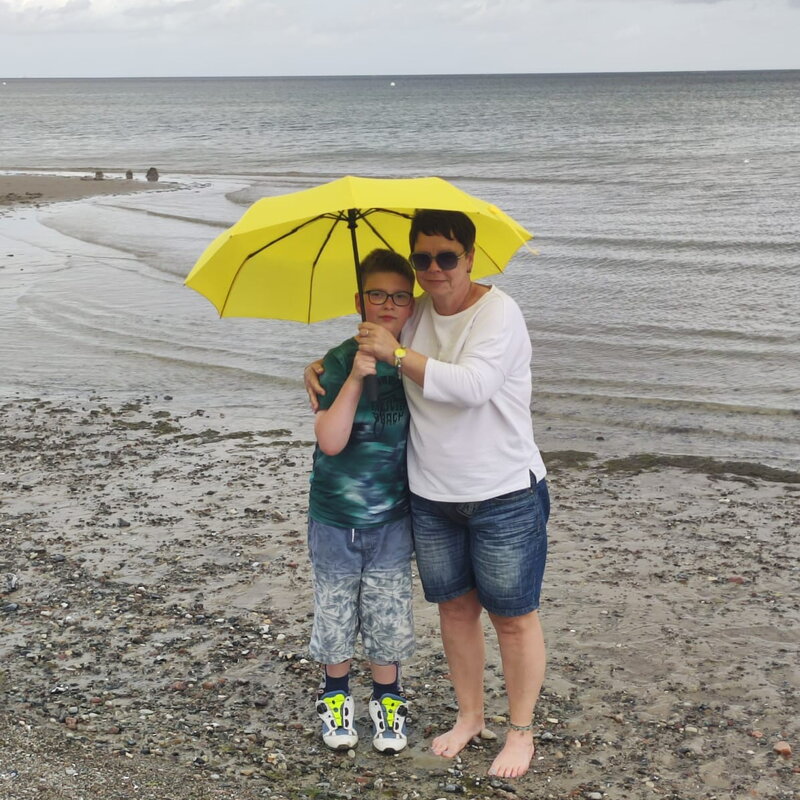 Eine Frau und ein Kind stehen unter einem gelben Schirm am Strand