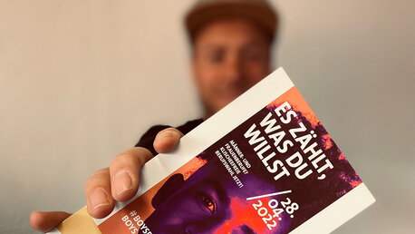 Ein Mann hält einen Flyer in die Kamera.