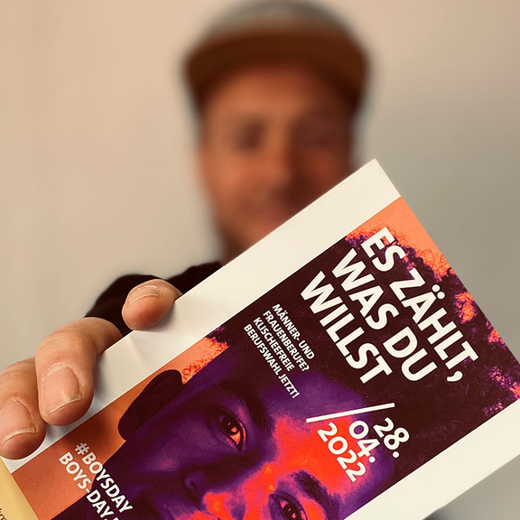Ein Mann hält einen Flyer in die Kamera.