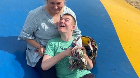Eine Frau und ein Junge sitzen zusammen auf einem Sprungkissen und lachen fröhlich.