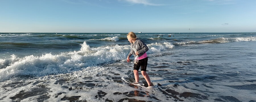 Ein Kind am Strand steht mit dem Füßen in den Wellen.