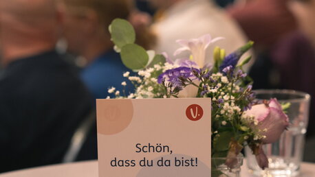 Tischschild steht in einem Saal vor einem kleinen Blumenstrauß