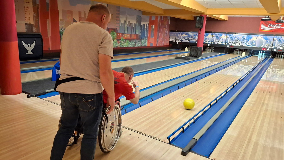 Zwei Männer, einer davon im Rollstuhl, auf einer Bowlingbahn