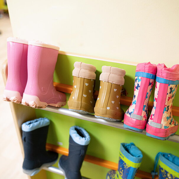 Mehrere Paare bunter Kindergummistiefel stehen ordentlich aufgereiht in einem Schuhregal der Kita. Die Stiefel zeigen verschiedene Muster wie Herzen und Schmetterlinge.